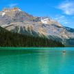 A tranquil lake in Canada with a majestic mountain in the background, surrounded by lush greenery