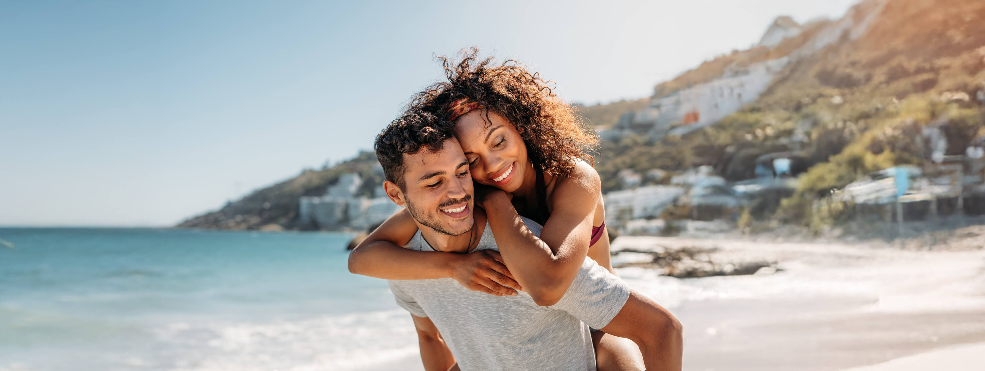 A couple embraces along a scenic beach with a rising cliff in the background.