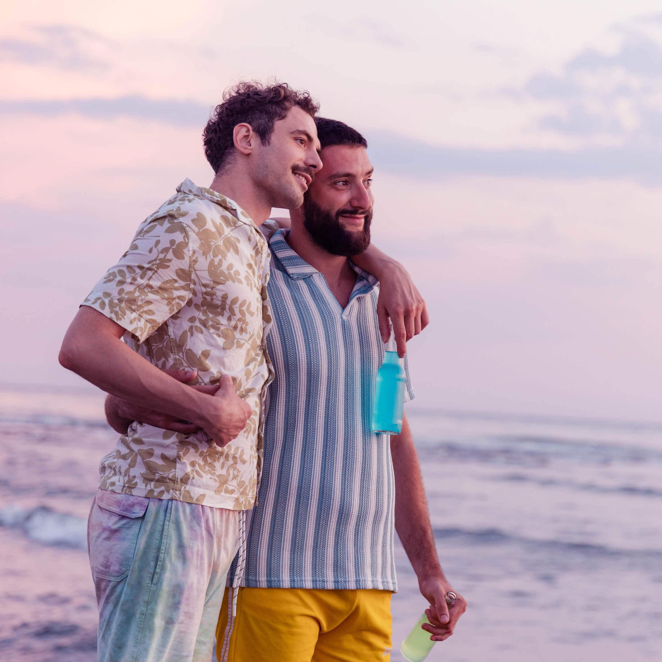A gay couple embrace with the ocean in the background